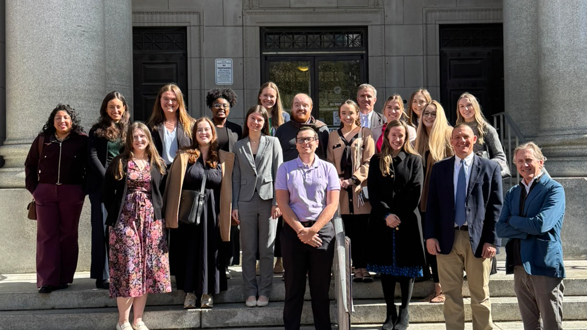 A large group pose for a photo on a set of stone steps in front of a building.