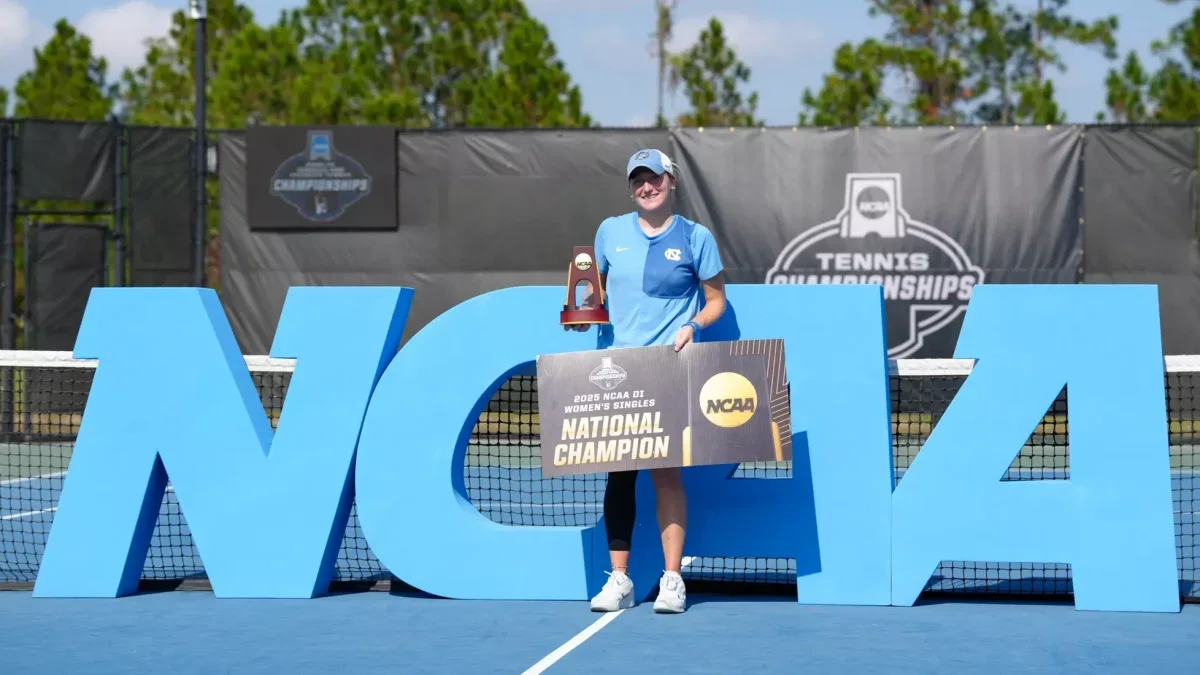 Reese Brantmeier holding her national championship trophy and holding a national champion sign on a tennis court.