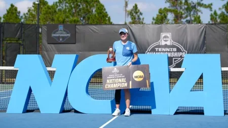 Reese Brantmeier holding her national championship trophy and holding a national champion sign on a tennis court.